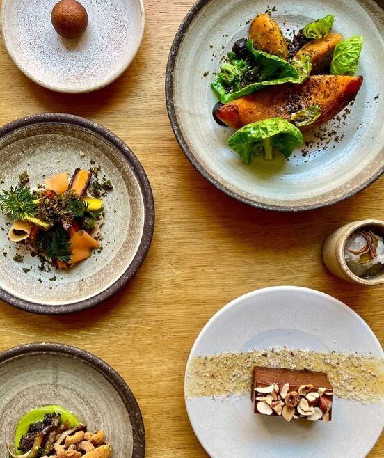 Image taken from above of the Apricity seasonal tasting menu with 5 plates and small cup including snacks and , vegetables and dessert